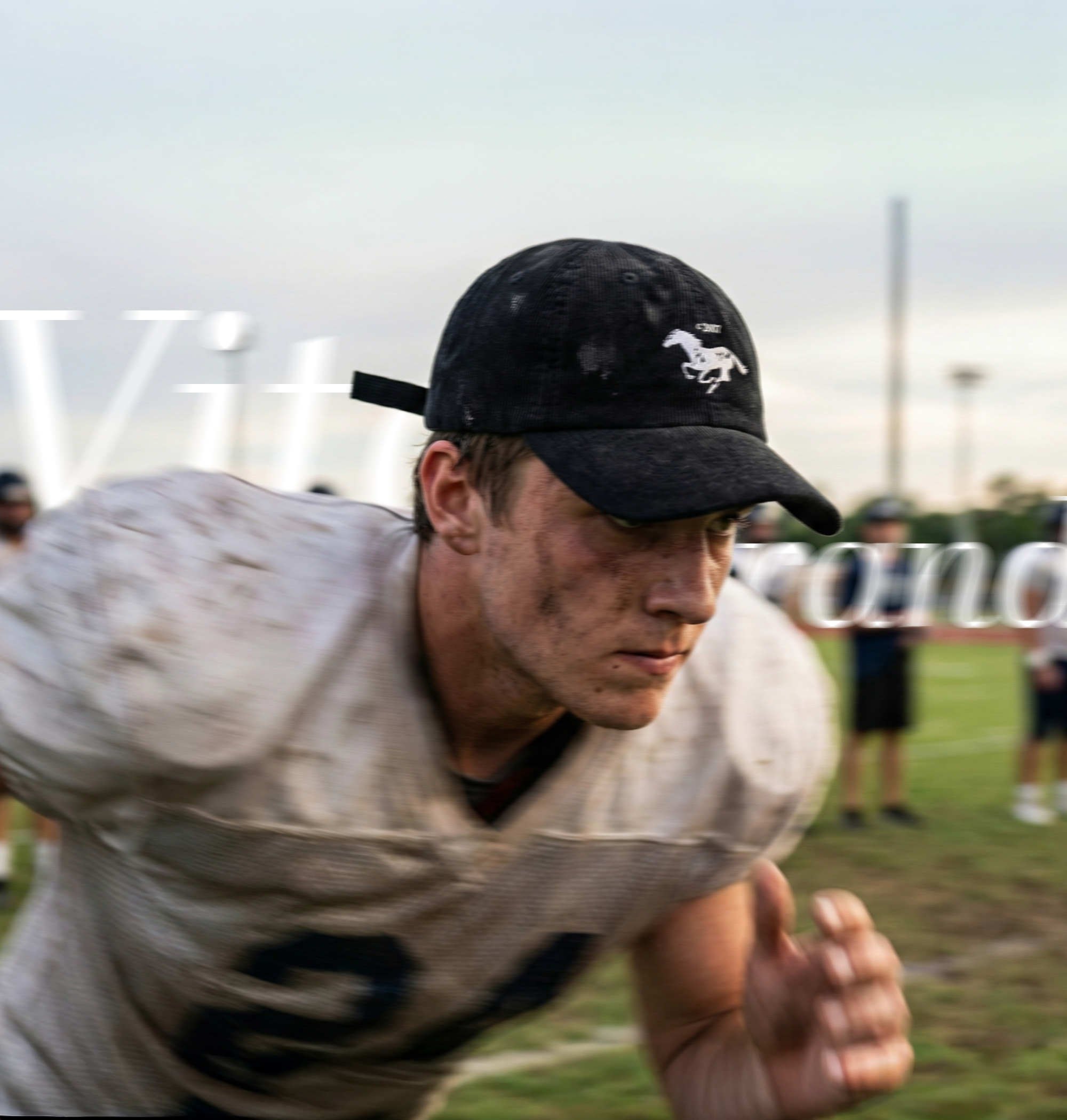 A young man wearing a black cap witha running mustang horse logo running in a football field