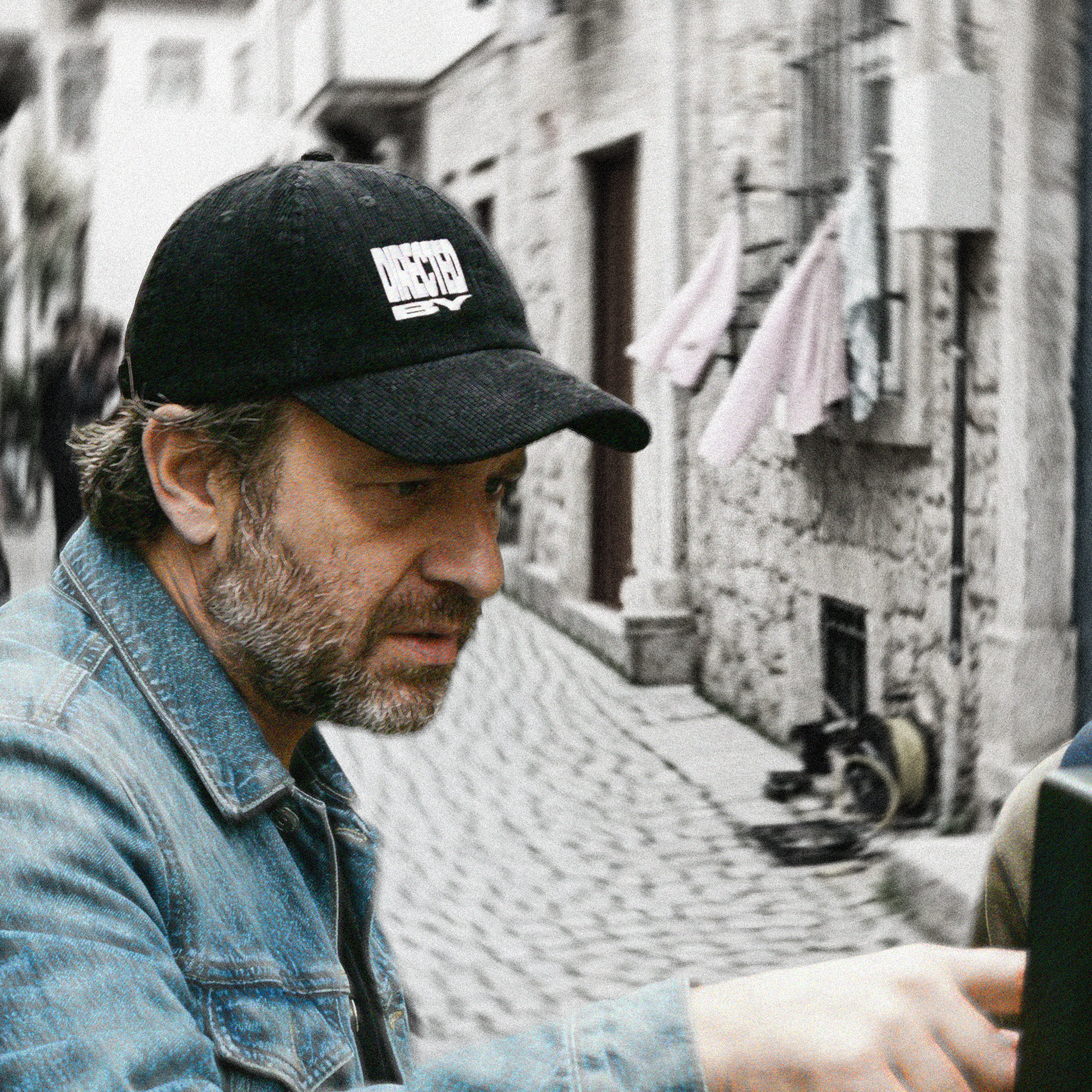 Man wearing a black cap with "DIRECTED BY" logo on a street.