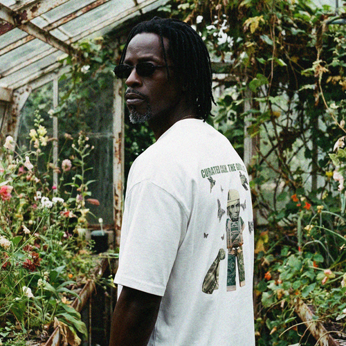 Person wearing a white t-shirt with graphics in a greenhouse setting "CURATED CASH. THE GOOD LIFE."