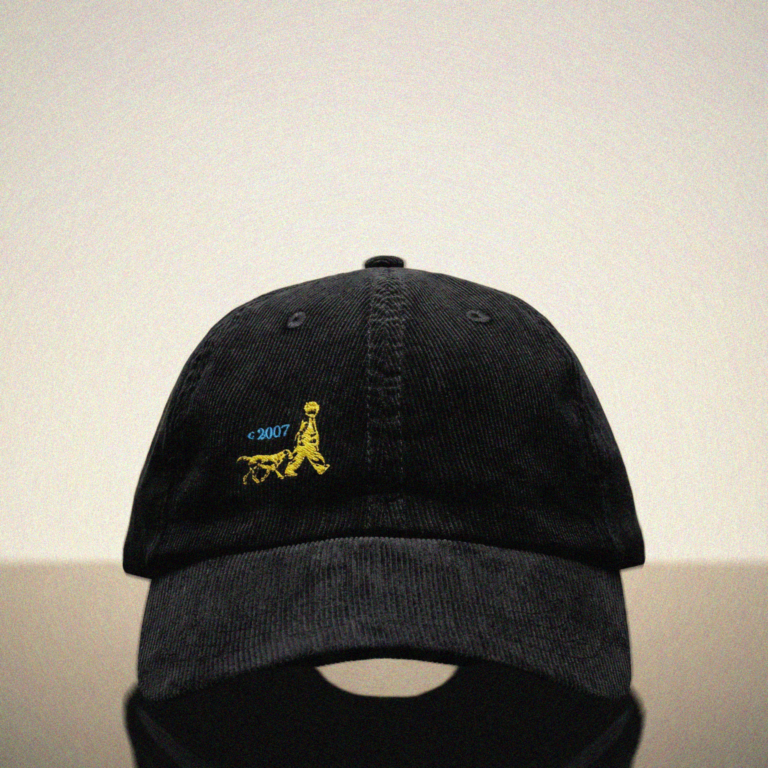 Black cap with yellow logo of a child and a dog on a reflective surface